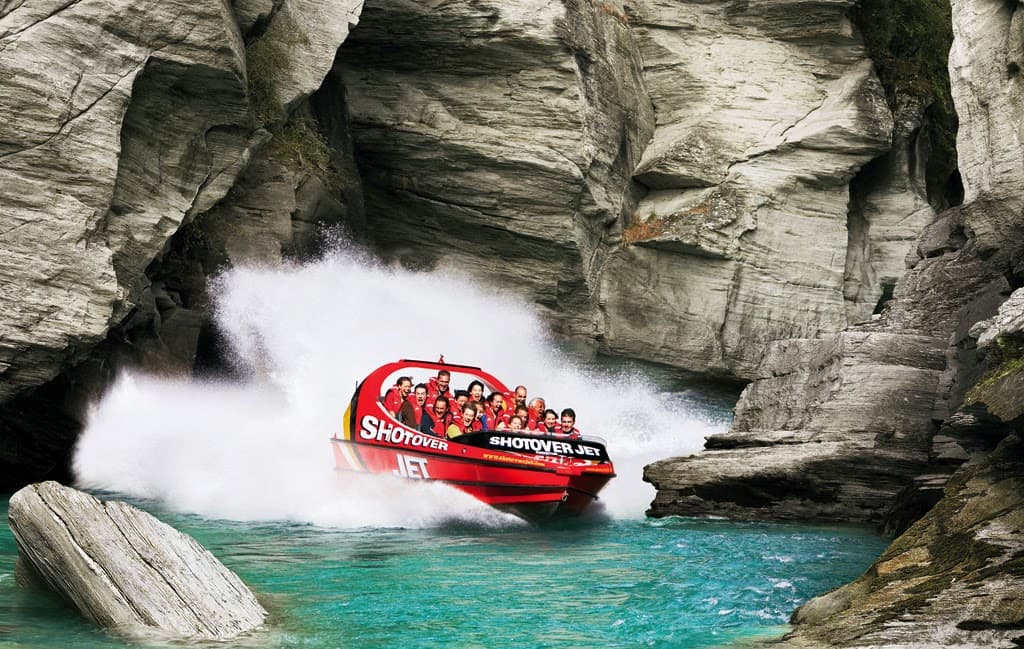 Red Shotover Jet boat speeding through narrow rock canyons on the Shotover River.