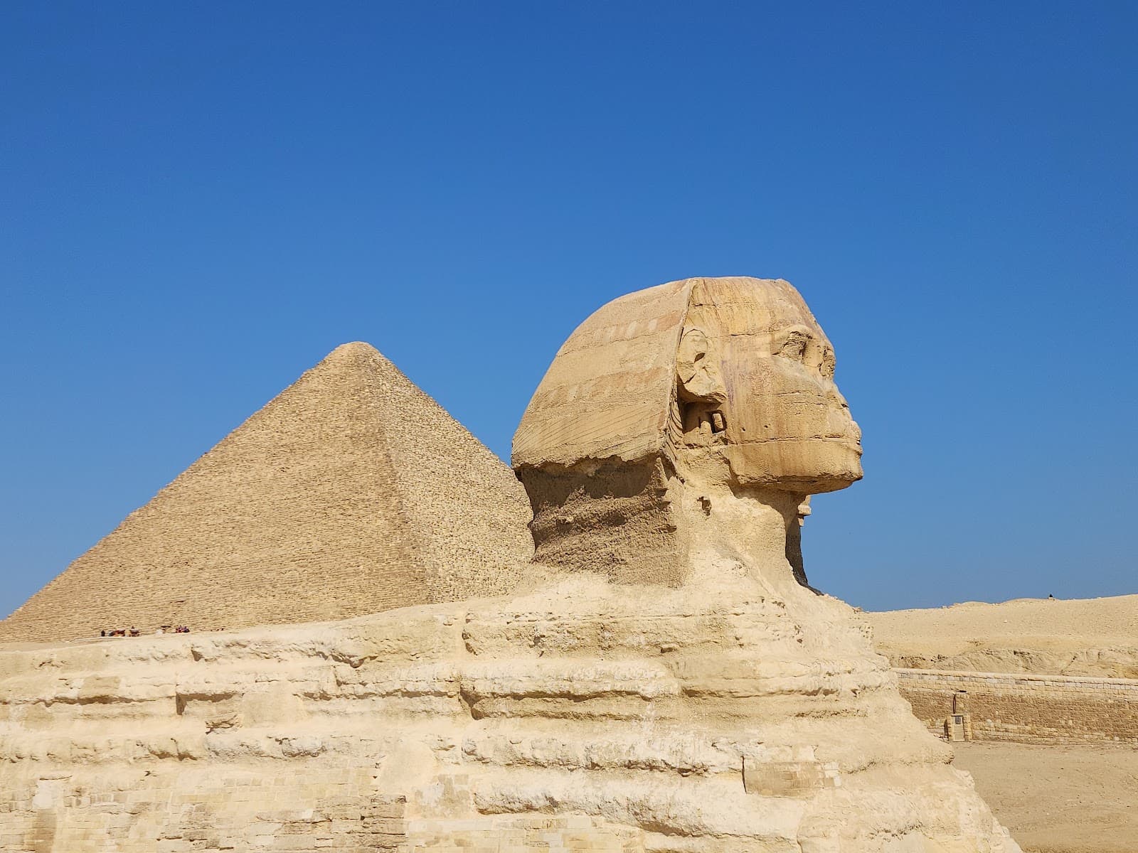تمثال أبو الهول العظيم وأحد الأهرامات تحت سماء زرقاء صافية.