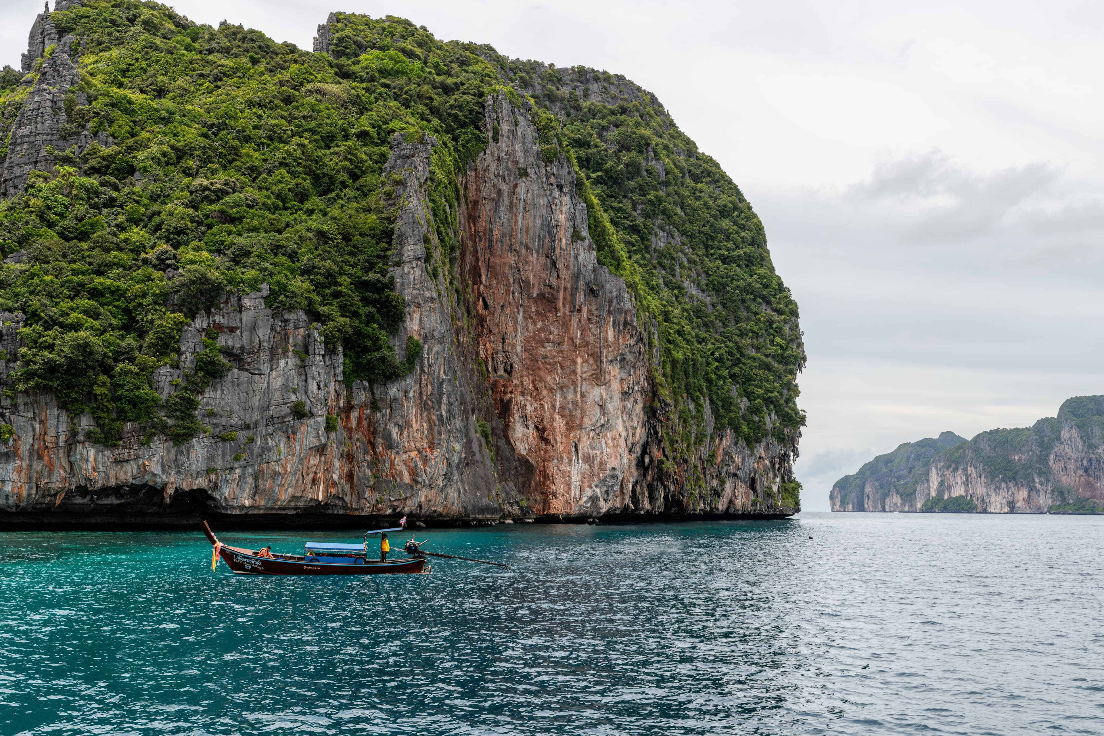 Longtail boat cruising past dramatic limestone karsts.