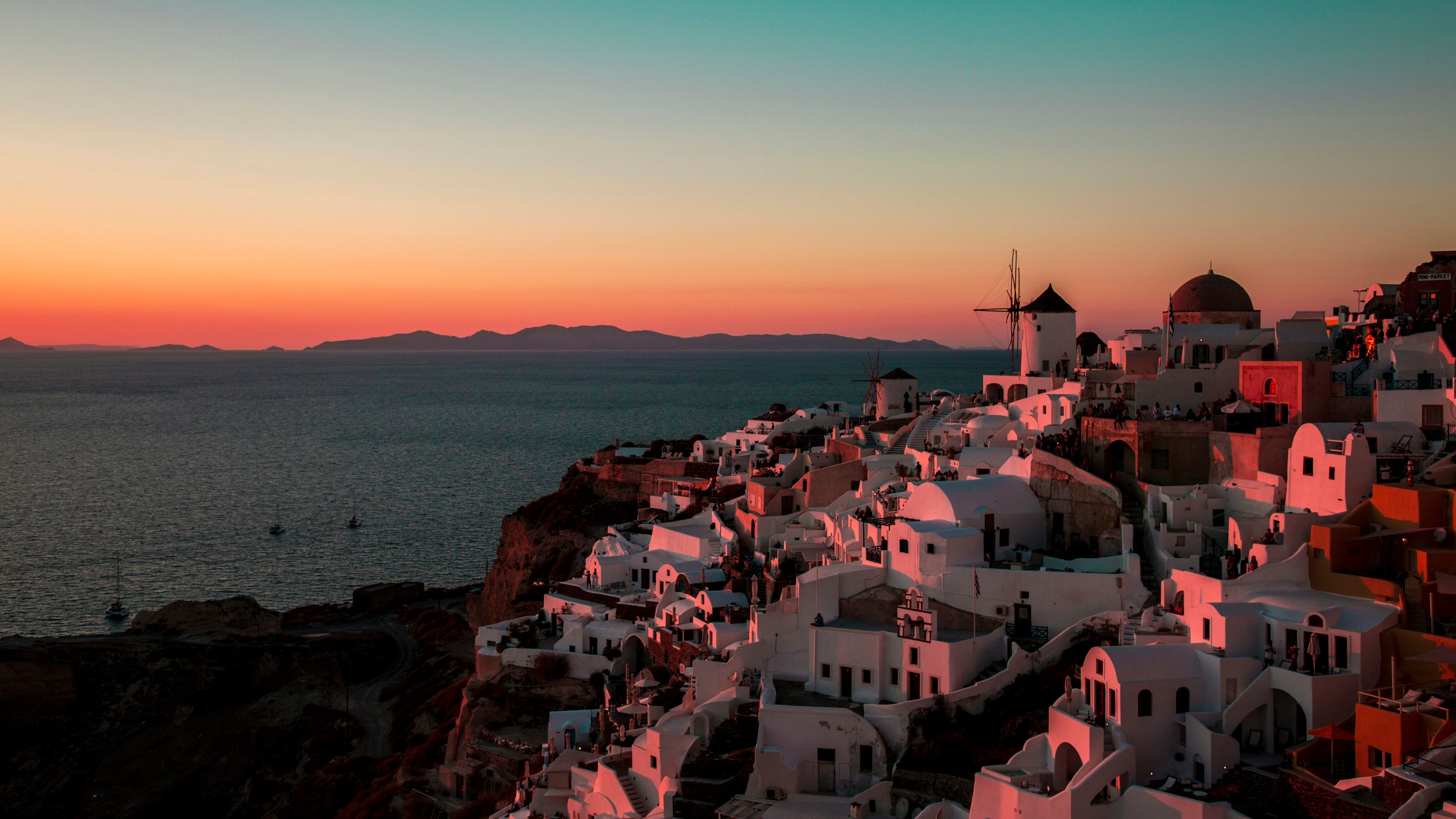 A breathtaking panoramic view of Oia village in Santorini during a vibrant sunset over the Aegean Sea.